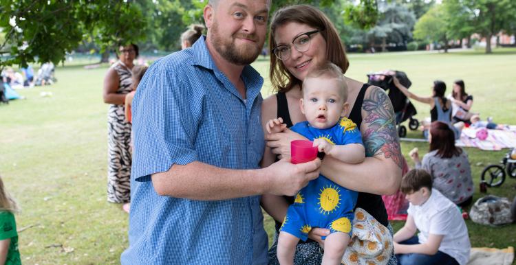 Picture of man and woman holding their baby at an outdoor event