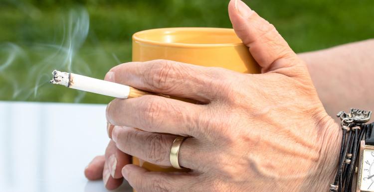 Close up a pair of hands wrapped around a mug holding a cigarette.