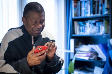 A man sitting at a desk in front of a bookcase, looking down at a mobile phone.