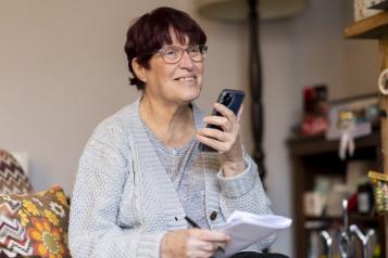 A smiling woman holding a smartphone and some pieces of paper.