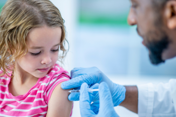 A young girl is indoors in a hospital room. She is being given a vaccine by her doctor.