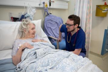 A nurse talking to an older woman in a hospital bed.