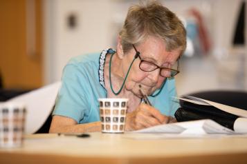 An elderley woman at a table writing on a piece of paper