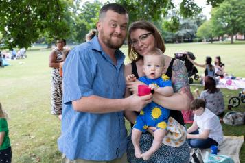 Picture of man and woman holding their baby at an outdoor event