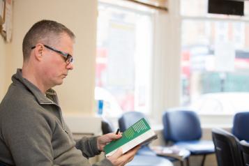 Middle aged man sitting in empty reception area of a GP reading a leaflet