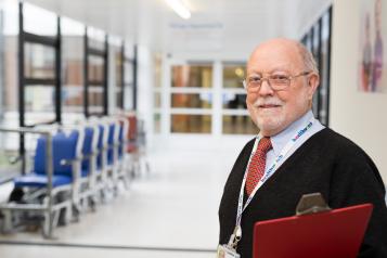 Man in a hospital corridor holding a clipboard