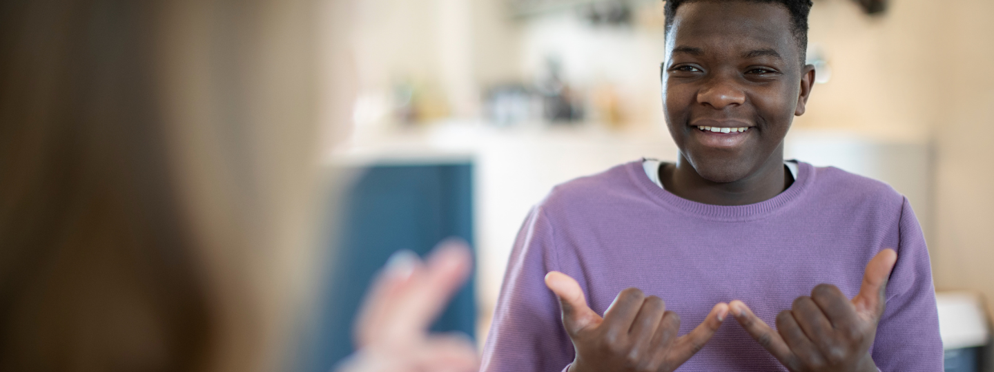A young person using sign language in conversation with another person.