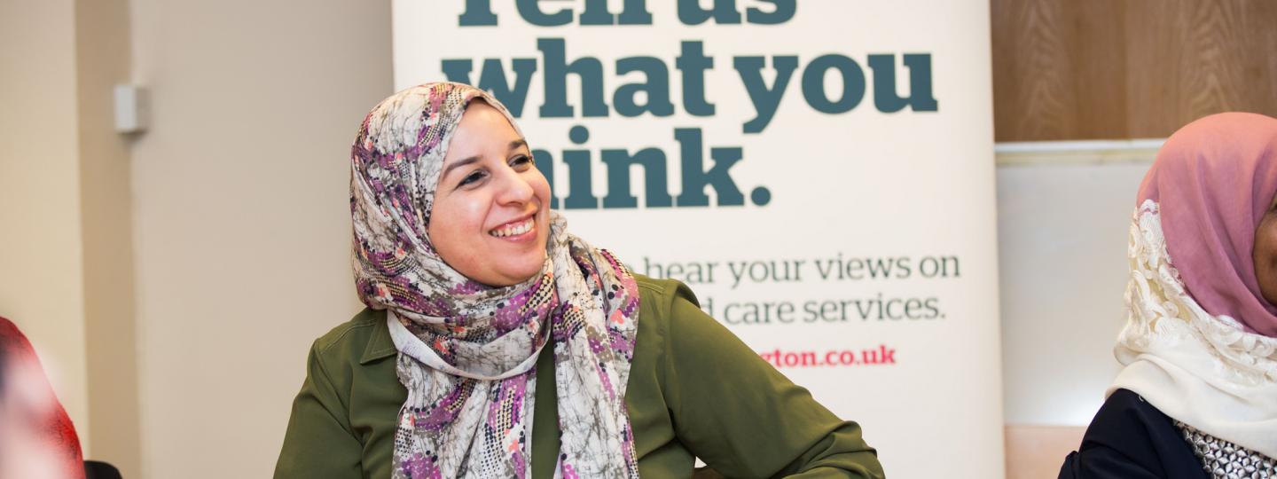 Woman in headscarf infront of a Healthwatch banner that says 'Tell us what you think'