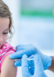 A young girl is indoors in a hospital room. She is being given a vaccine by her doctor.