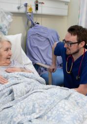 A nurse talking to an older woman in a hospital bed.